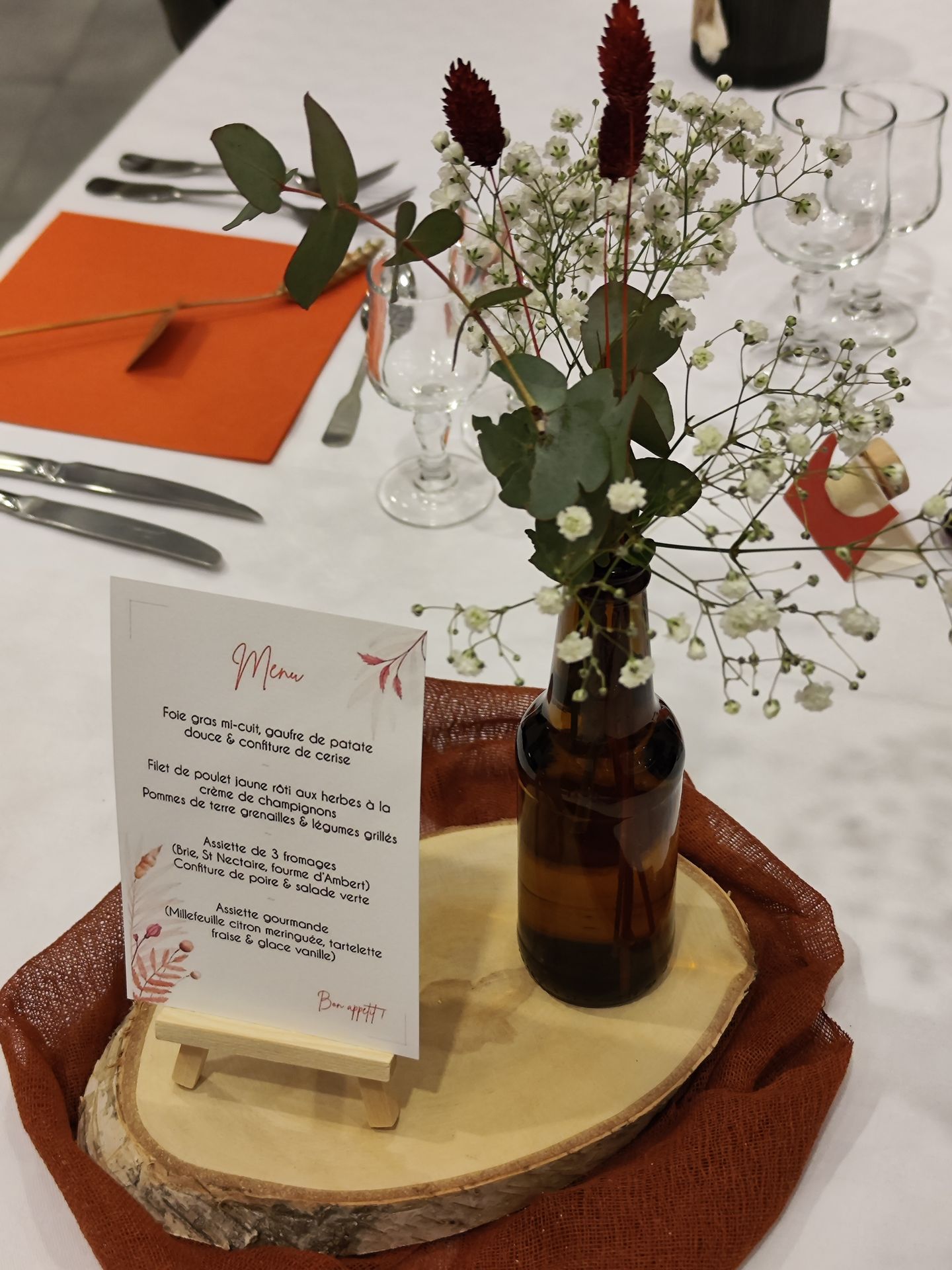 Mariage Espace Galerne table blanche hemin de table terracotta rondin en bois composition florale serviette orange bougie cadeaux invités bouchon de vin menu de table sur socle en bois marque place épis de blé