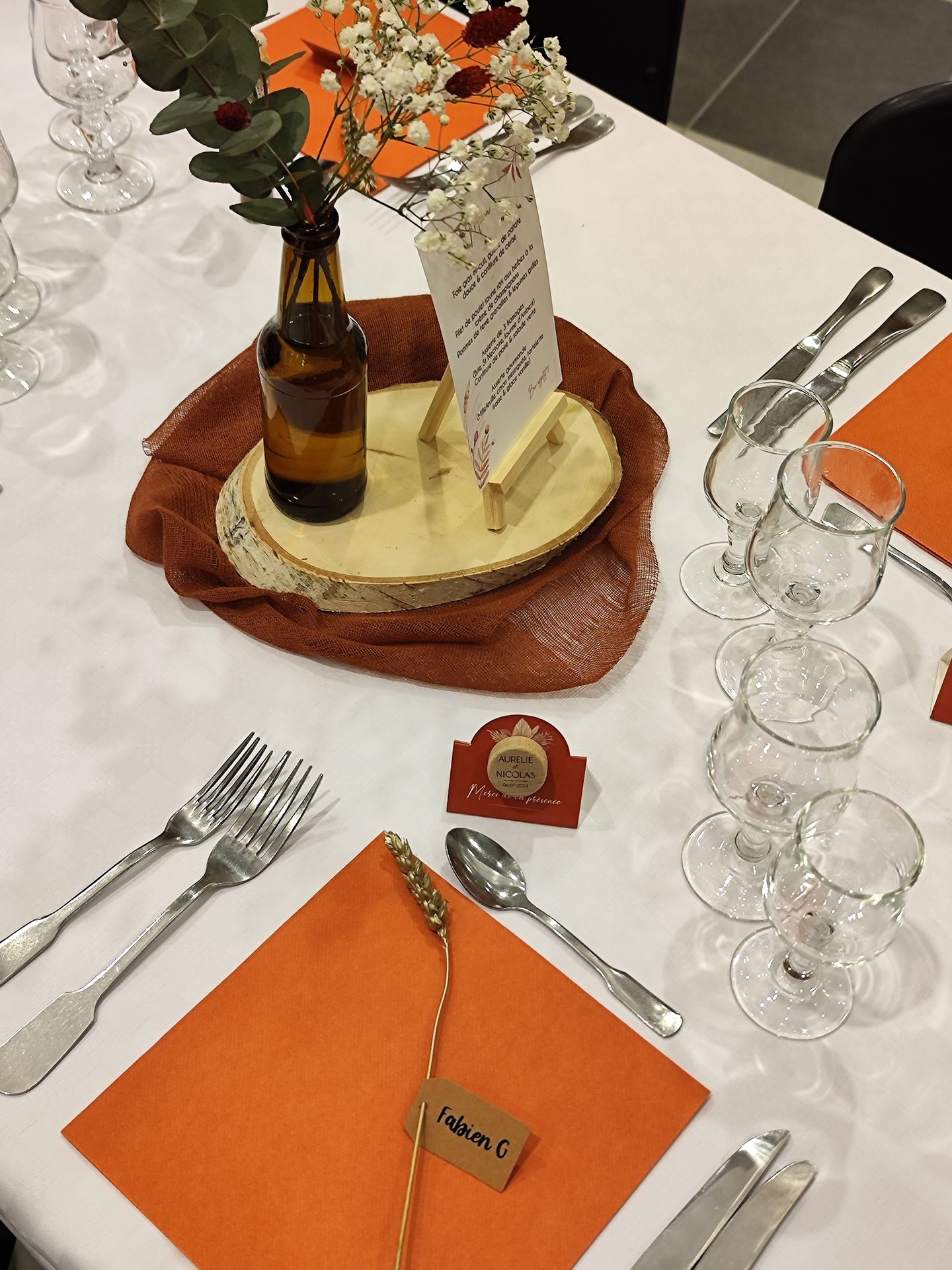 Mariage Espace Galerne table blanche hemin de table terracotta rondin en bois composition florale serviette orange bougie cadeaux invités bouchon de vin menu de table sur socle en bois marque place épis de blé