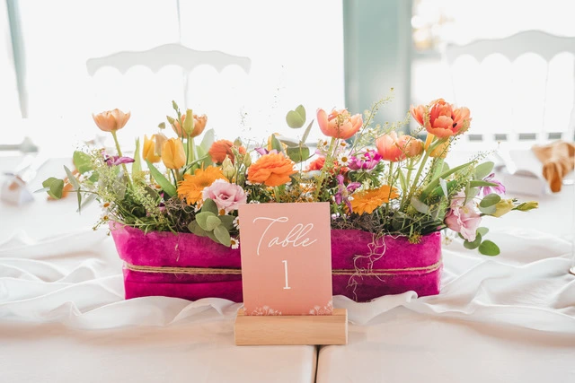 Mariage Domaine de la Sapinière compositions florales dans un pot rose vif nom de table sur socle en bois
