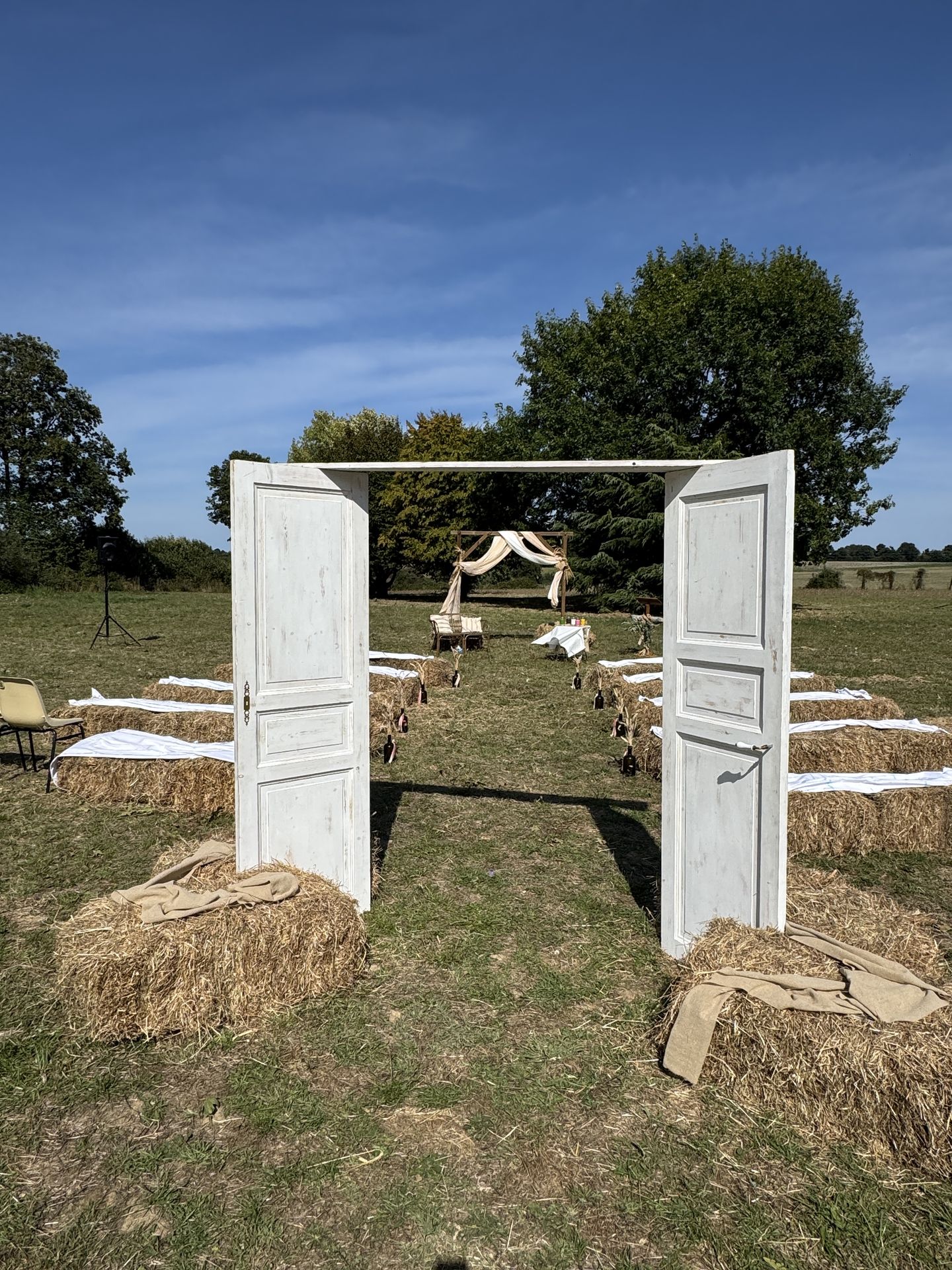 Renouvellement de voeux La pétinière Cérémonie extérieure porte en bois blanc botte de paille et tissu blanc arche en bois et tissu sable et blanc