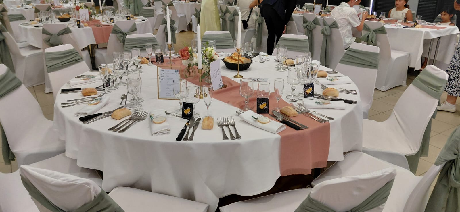 Mariage La Thèvinière tables blanches noeuds de chaises vert sauges et chemin de table vieux rose bougies cadre menu doré