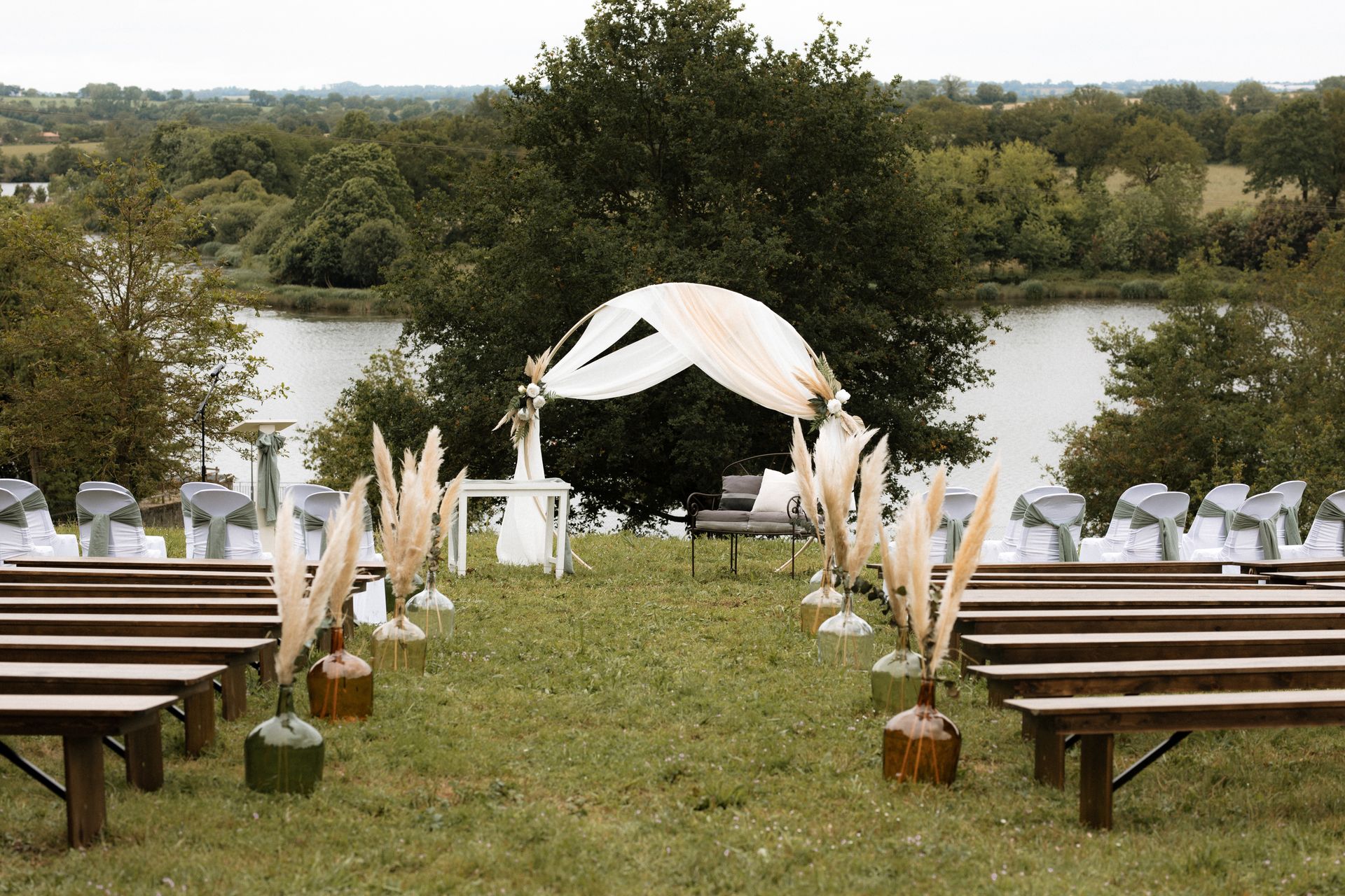 Mariage Salle de la Goubaudière cérémonie laique extérieure vase couleur pamaps arche tentures blanc chaises blanches noeuds vert sauge