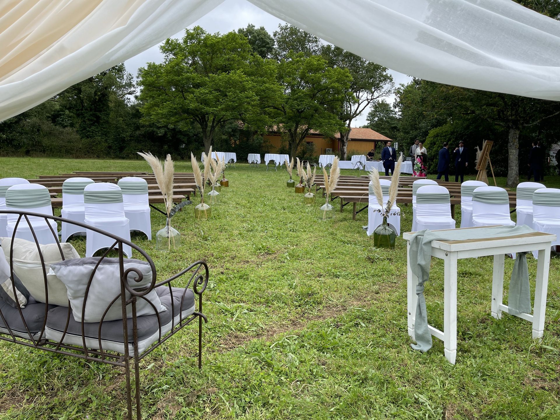 Mariage Salle de la Goubaudière cérémonie laique extérieure vase couleur pamaps arche tentures blanc chaises blanches noeuds vert sauge