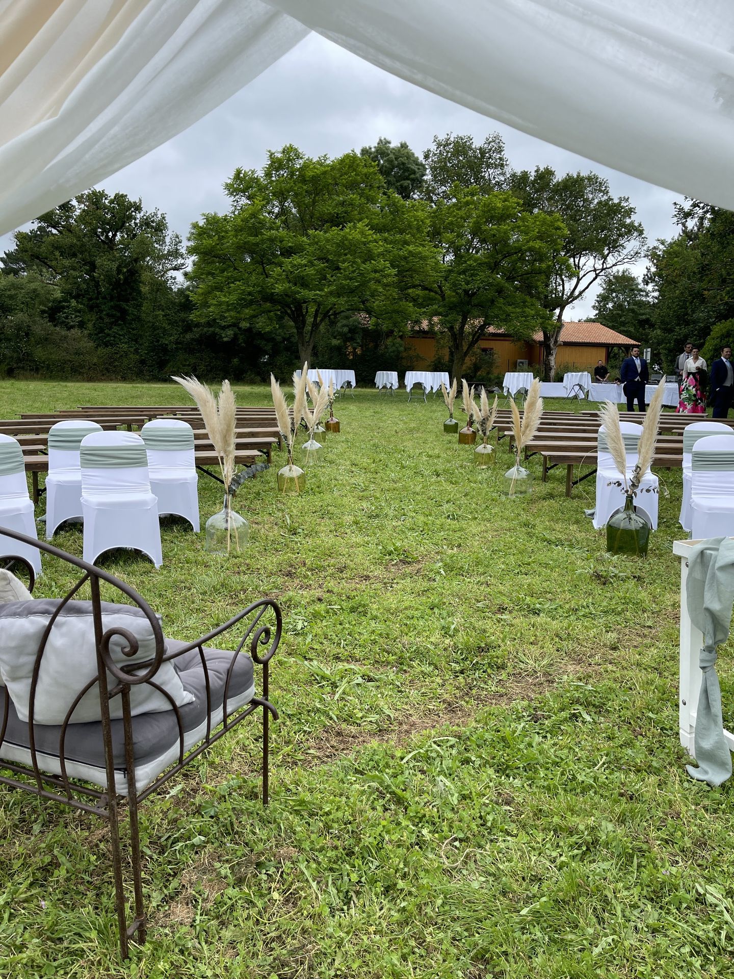 Mariage Salle de la Goubaudière cérémonie laique extérieure vase couleur pamaps arche tentures blanc chaises blanches noeuds vert sauge