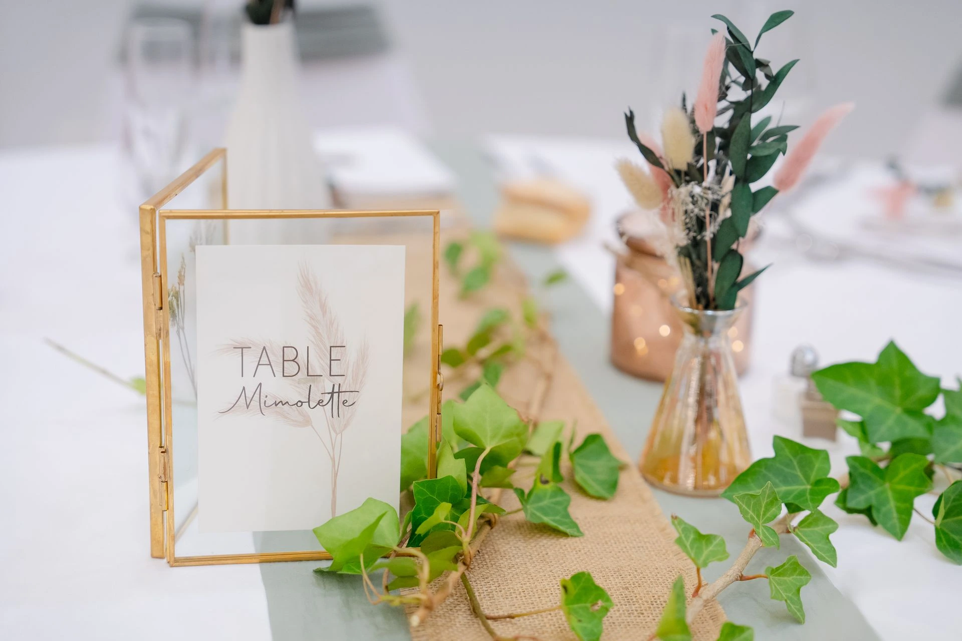 Mariage la thévinière  table blanche chemin de table vert sauge et  sable nom de table cadre dorée vase fleuris feuille lière