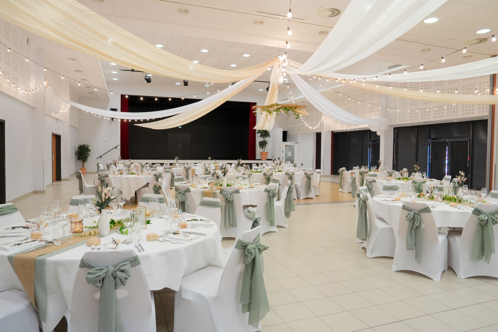 Mariage la thévinière salle intérieure plafond tentures blanches et sables tables blancheschaises noeuds vert sauge