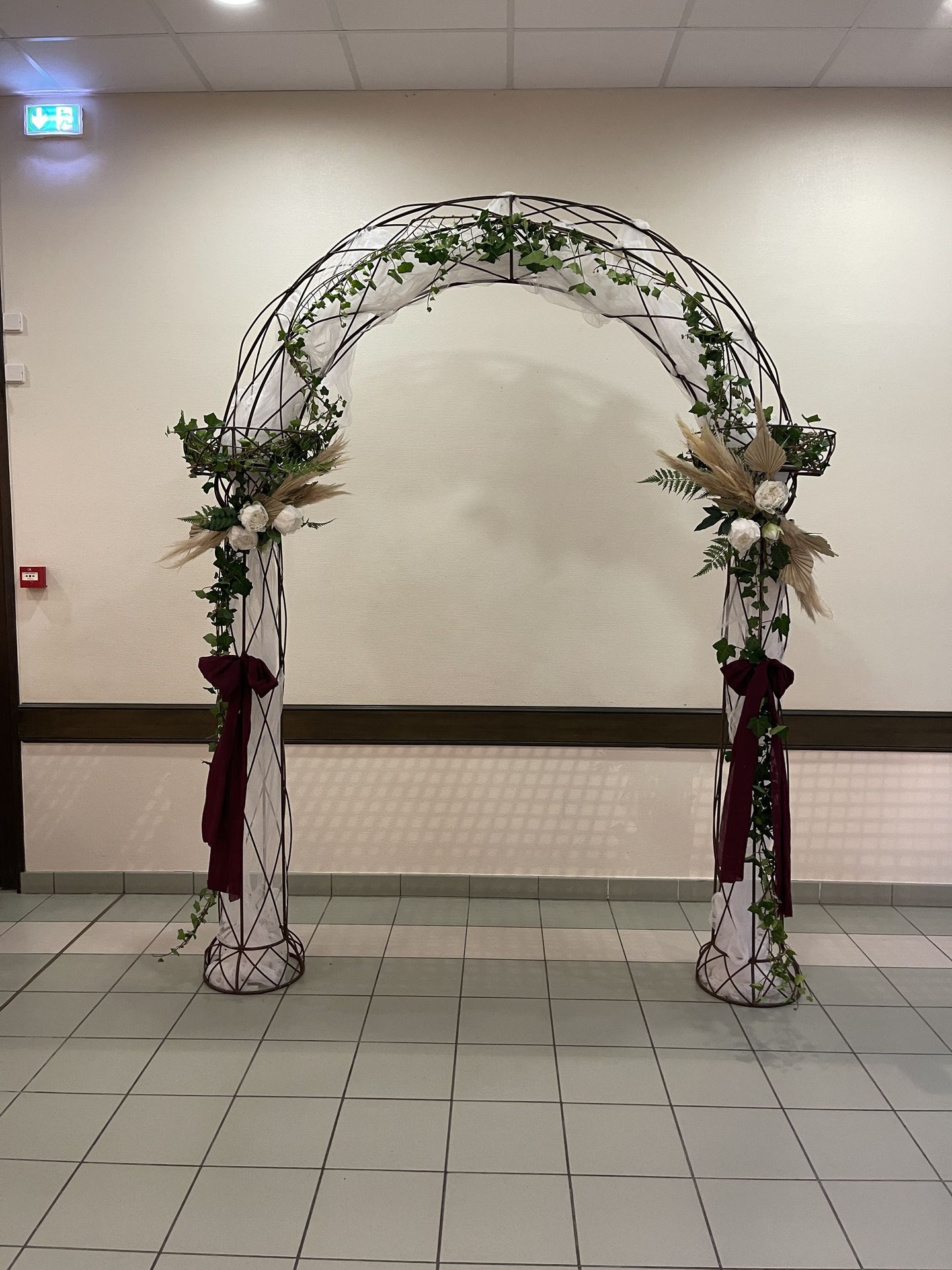 Mariage Salle le Lys arche arrondi tissu blanc noeud bordeaux lière composition florale