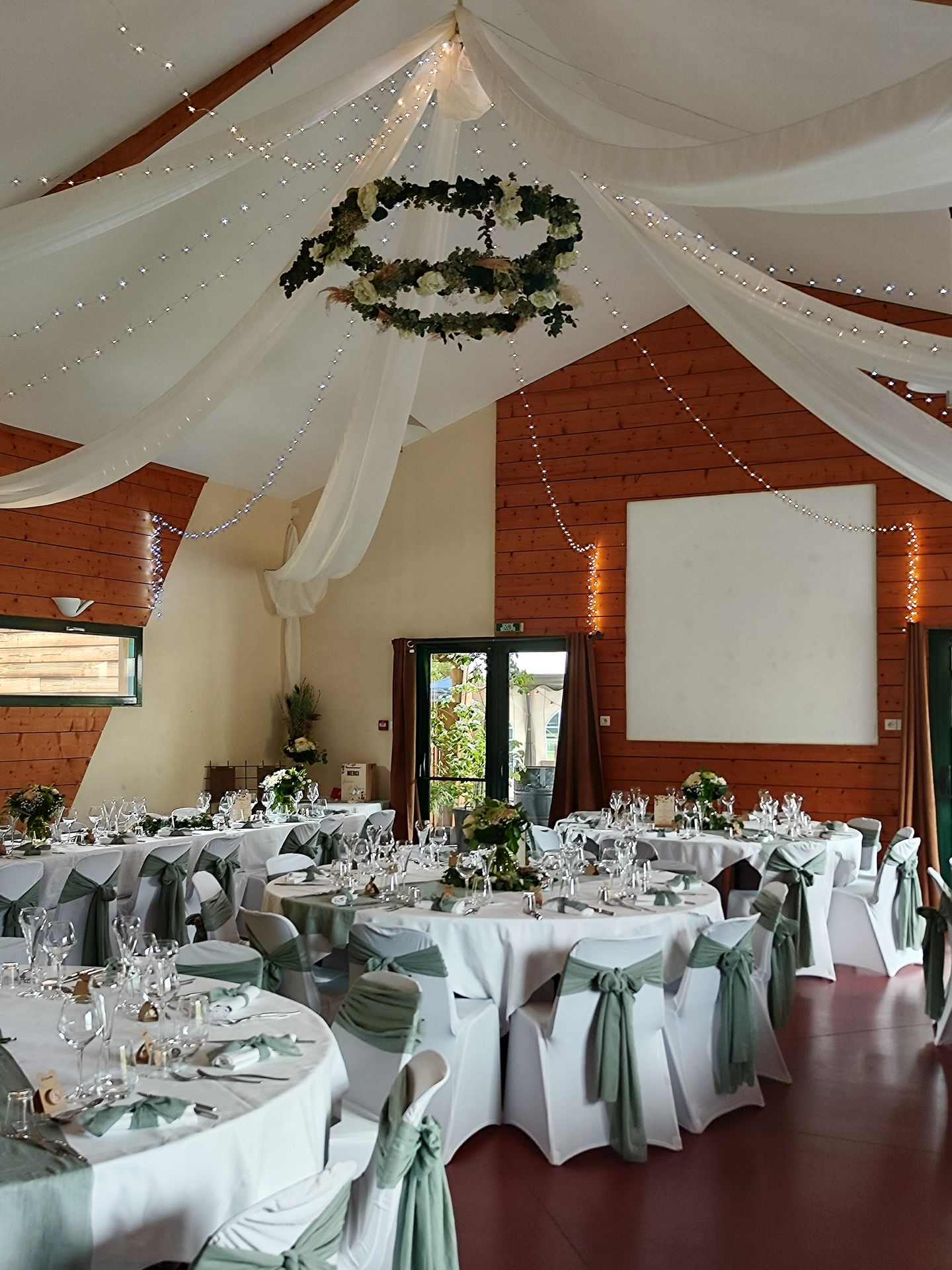 Mariage Ter'Anima salle intérieure plafond tentures blanches leds couronnes fleurs table blanches chaises blanche noeud vert fleurs
