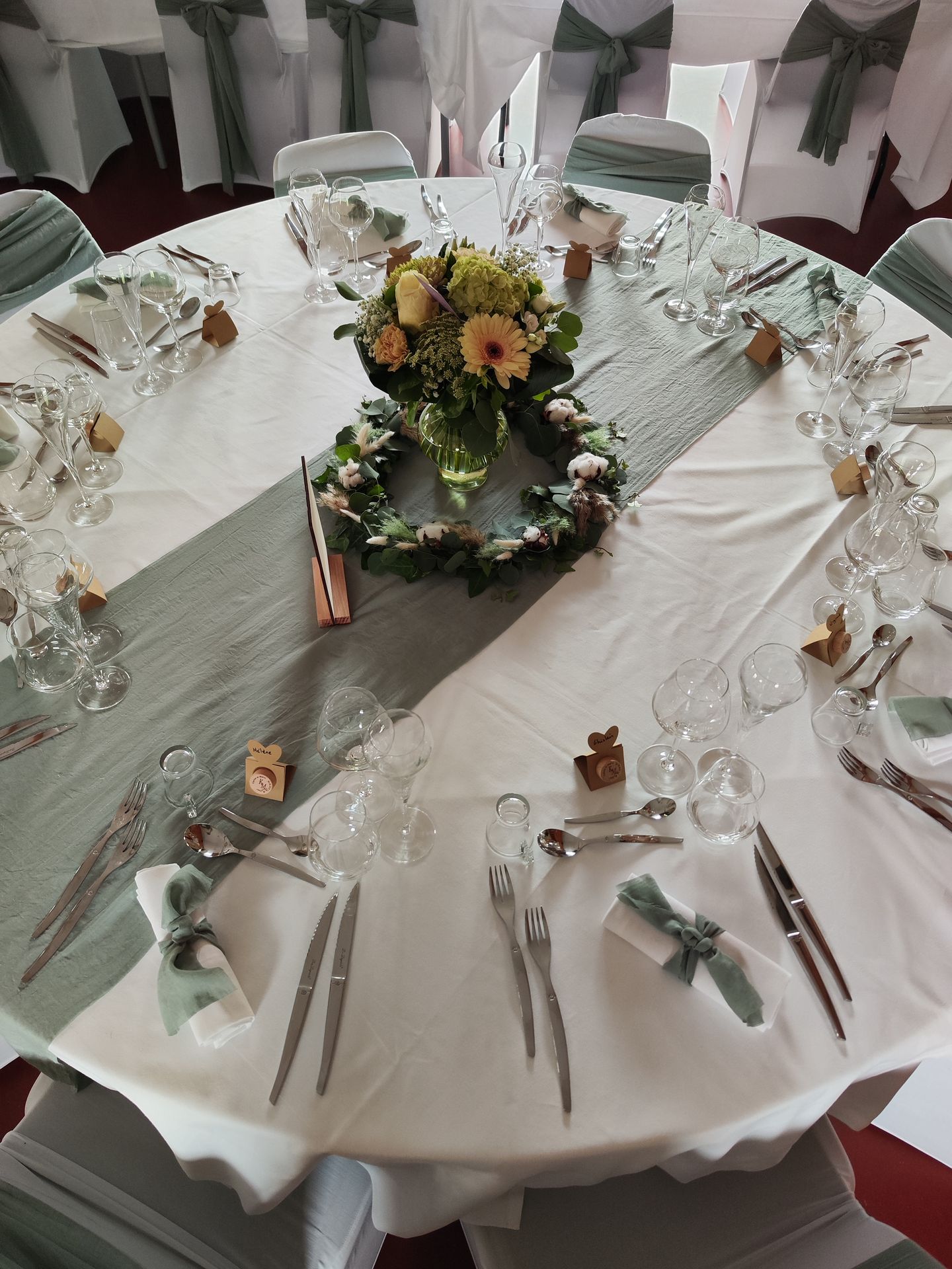 Mariage Ter'Anima tables blanches noeud de chaise et chemin de table vert sauge composition florales cadeaux invités bouchon de vin menu en bois