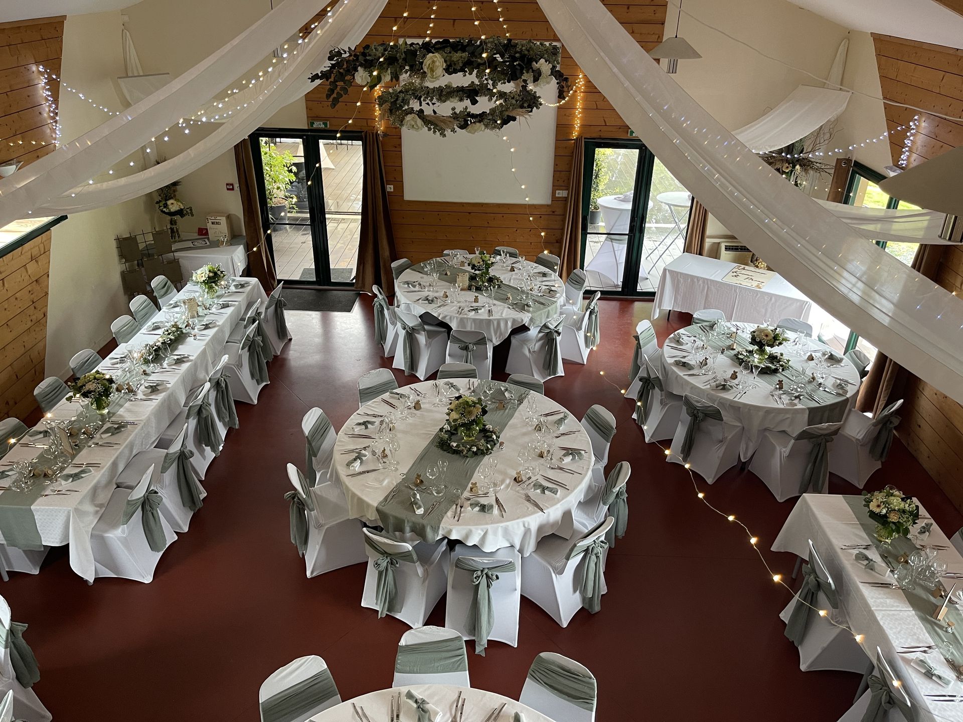 Mariage Ter'Anima salle intérieure plafond tentures blanches leds couronnes fleurs table blanches chaises blanche noeud vert fleurs