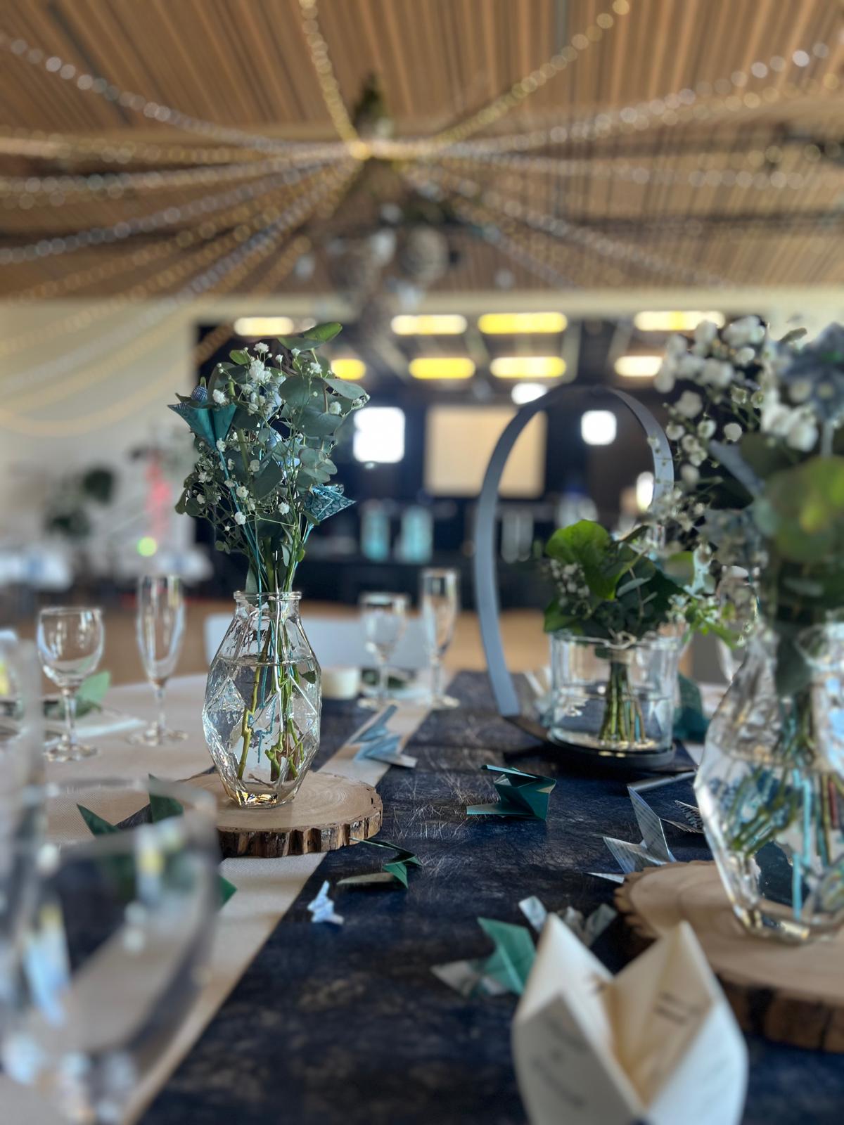 Mariage La Prairie vase transparent composition florales feuillage fleurs bleu rondin en bois coeur noir