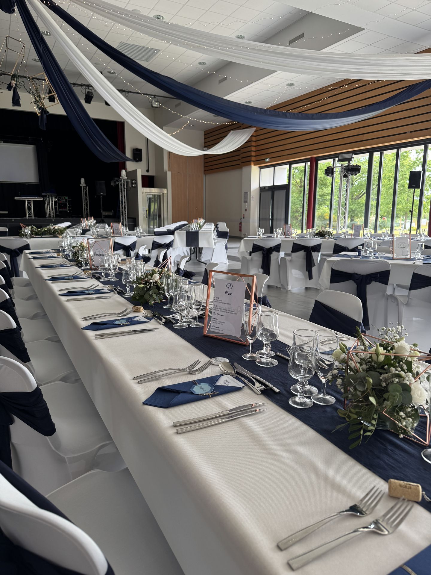 Mariage Espace Galerne plafond tentures bleu et blanc leds table blanche chemin de table bleu marine composition florales menu cadre dorée