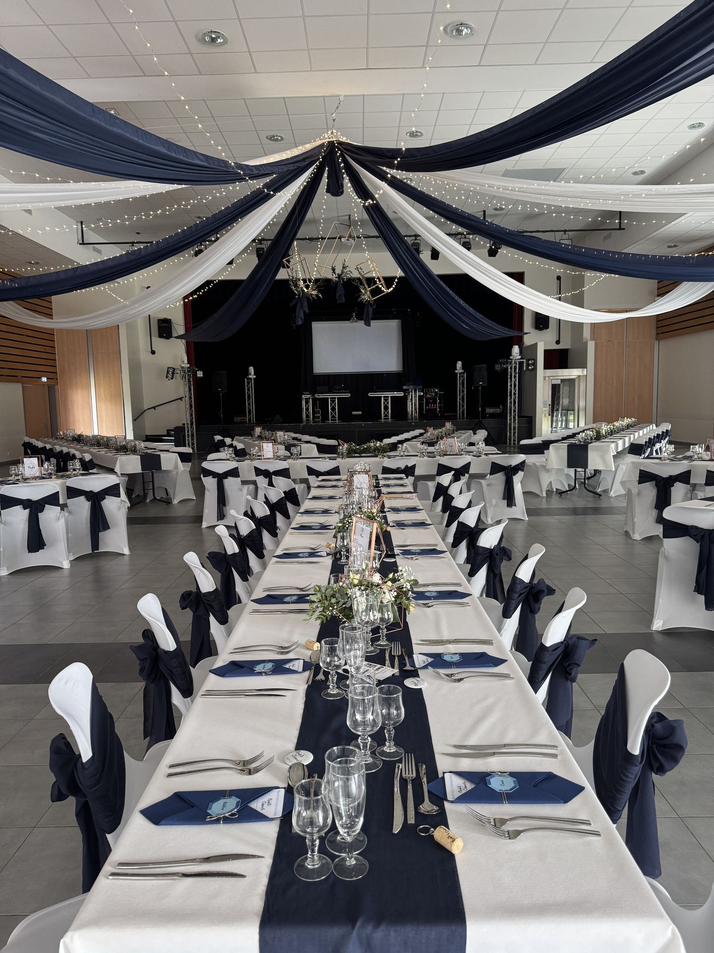 Mariage Espace Galerne plafond tentures bleu et blanc leds structures dorée feuillage table blanche chemin de table bleu marine et noeud de chaise