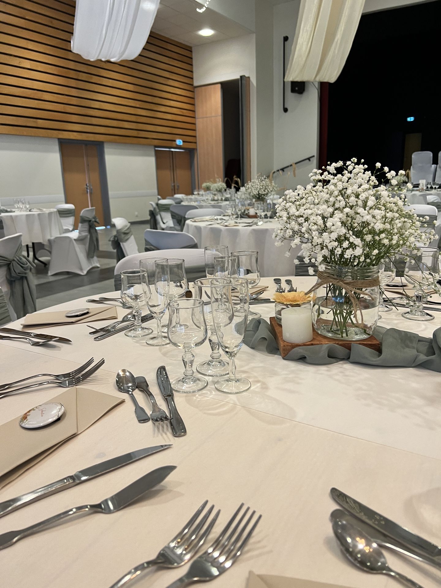 Mariage Espace Galerne table blanche noeud de chaise vert sauge centre de table vert sauge fleurs blanches menu de table sur brique fleurs orange serviette sable