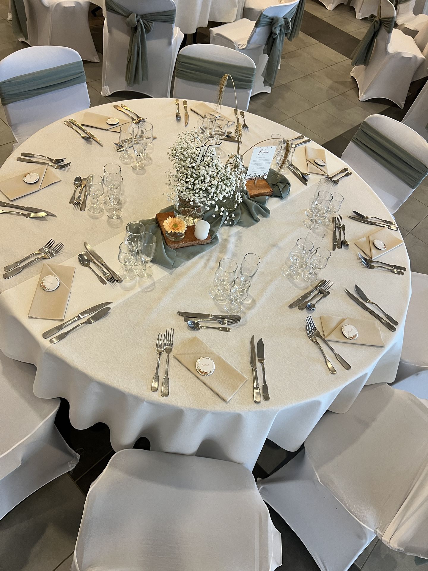 Mariage Espace Galerne table blanche noeud de chaise vert sauge centre de table vert sauge fleurs blanches menu de table sur brique fleurs orange serviette sable