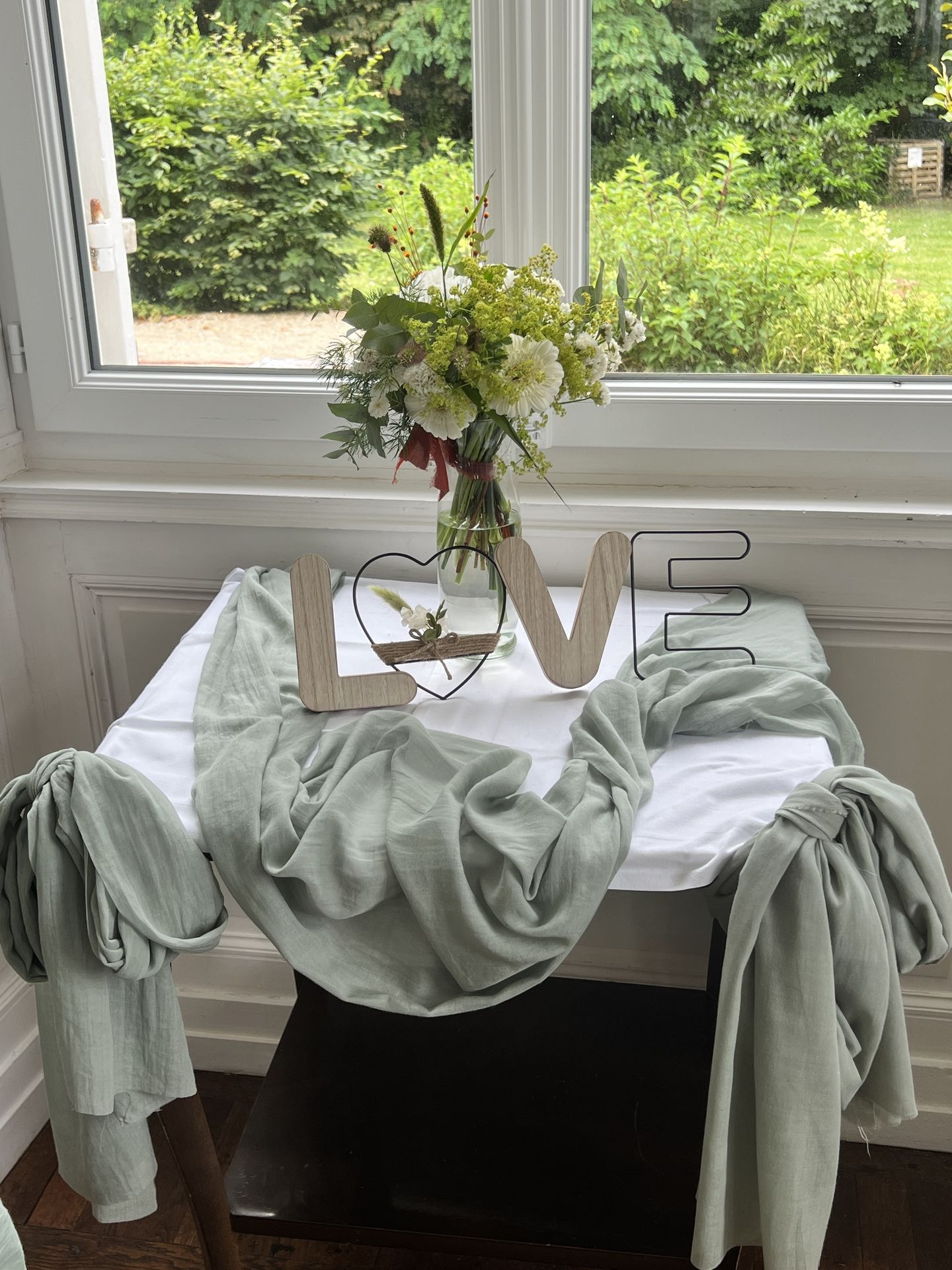 Mariage Château de la Forêt décor table nappe blanche tissu vert sauge love en bois et fer vase bouquet de fleurs