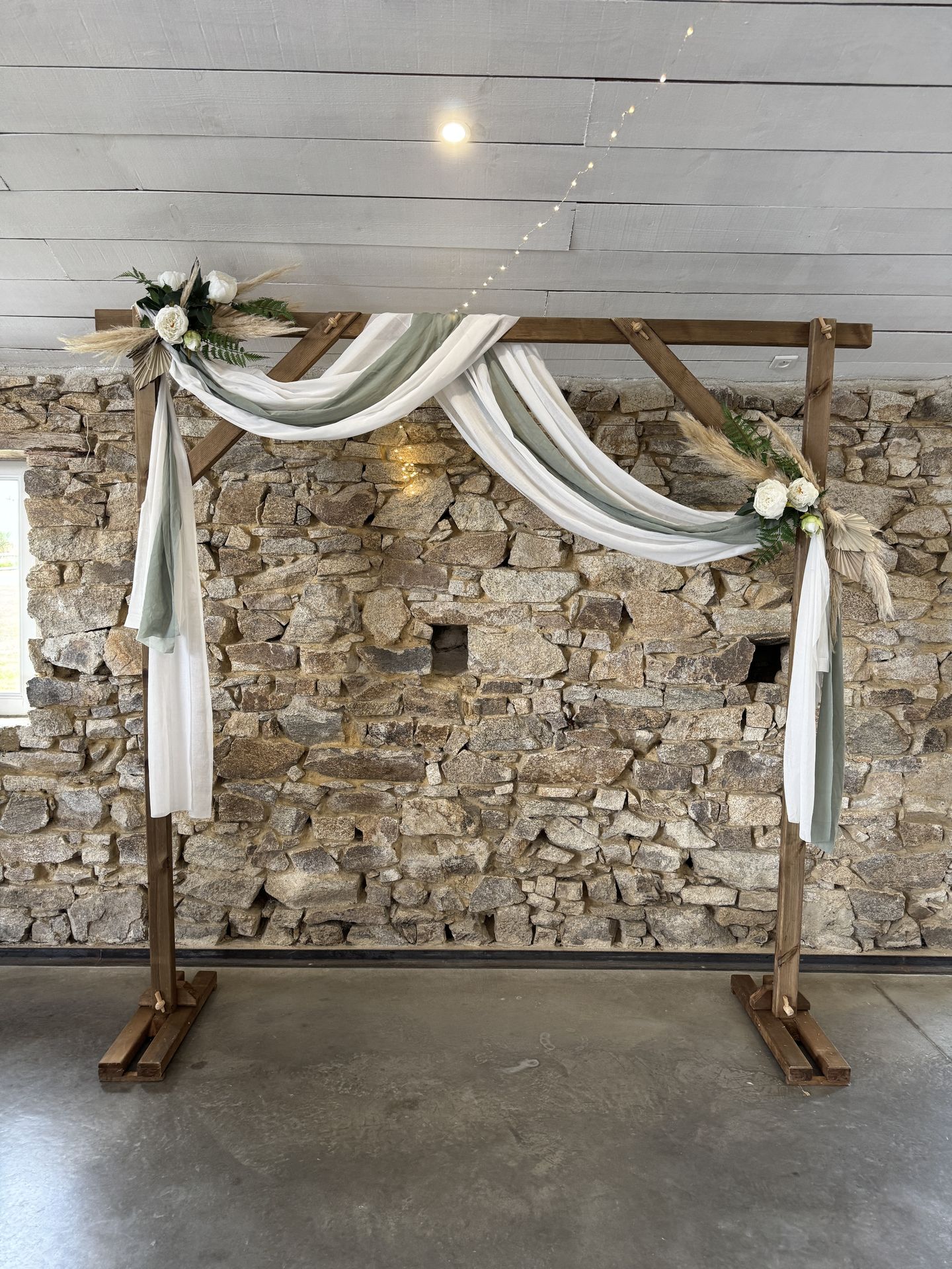 Mariage Domaine de Marin arche en bois tissu vert sauge et blanc composition feuillage pampas
