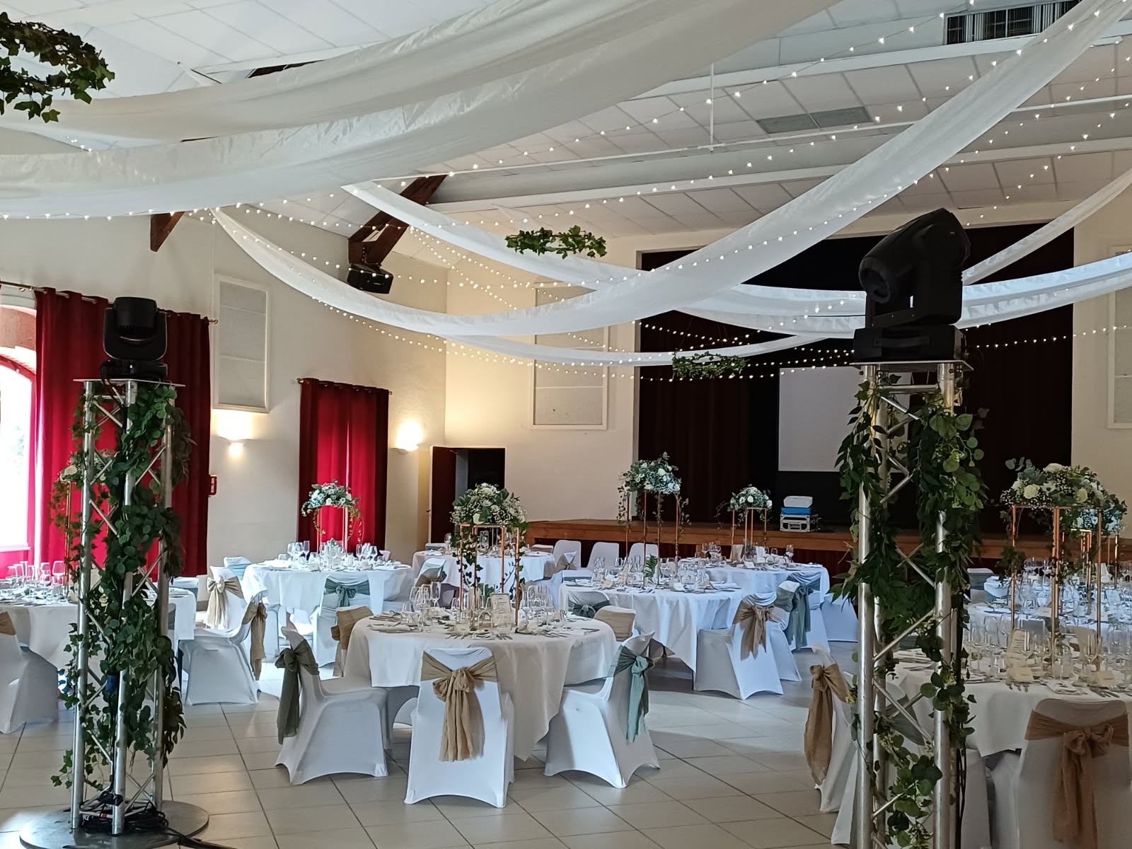 Mariage Salle des Fêtes salle intérieure table blanche chaise blanche noeud sable et vert sauge plafond tentures blanches et leds composition florale