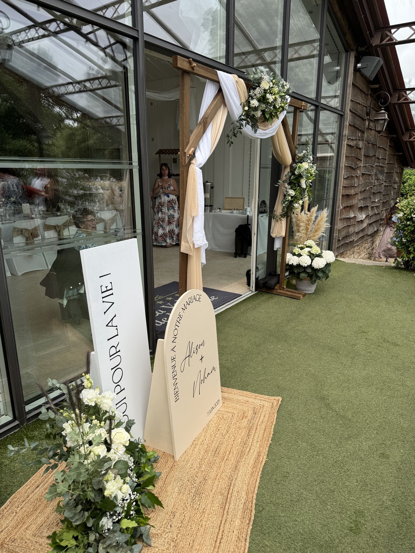 Mariage La Vallée de la Roche entrée salle panneau de bienvenue sable et blanc tapis en maille arche en bois tissu blanc et sable composition florale