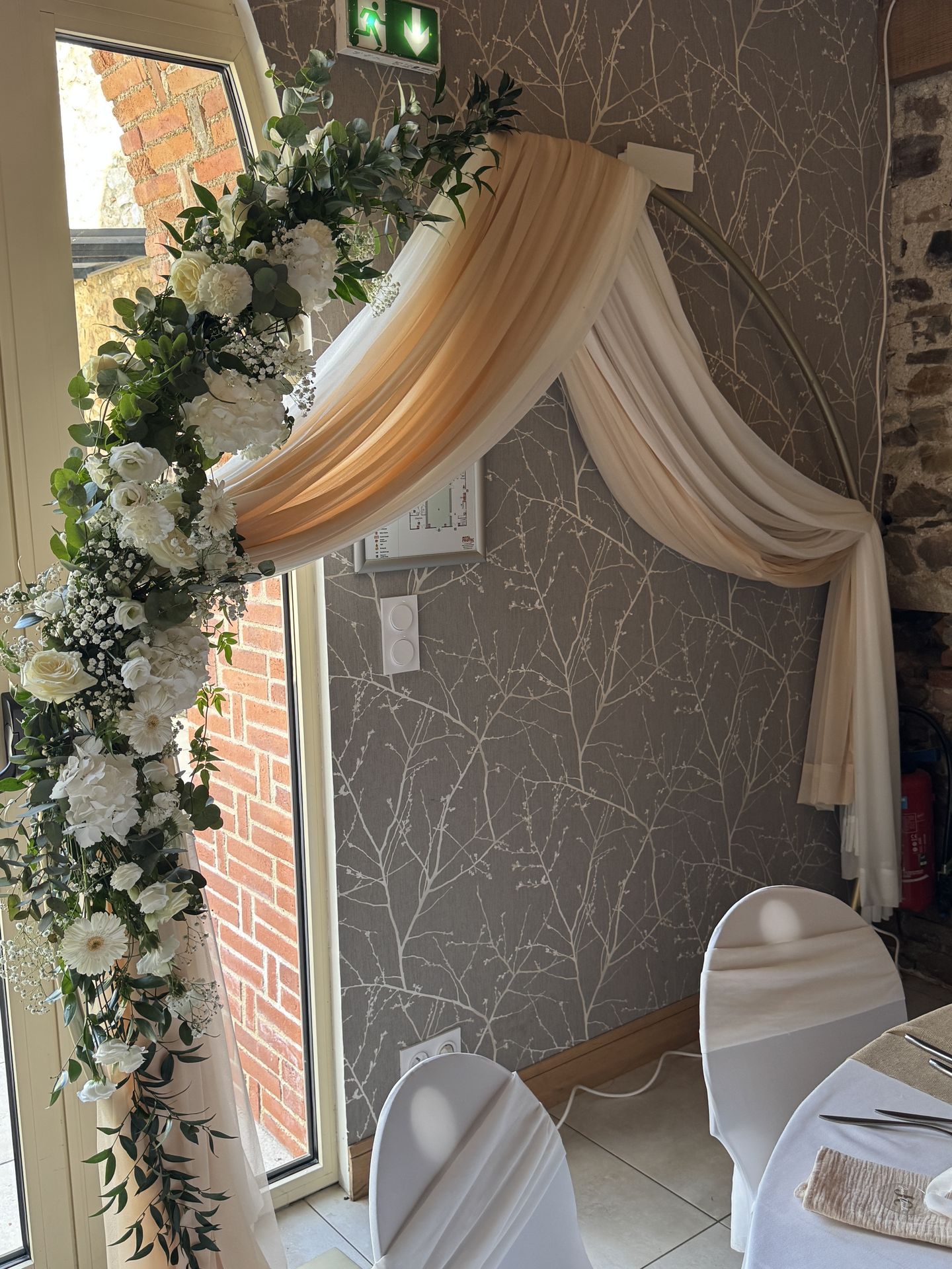 Mariage Domaine de Marin arche dorée ronde tissu blanc et sable composition florale