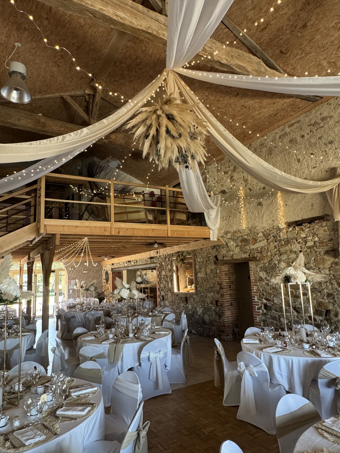 Mariage Domaine de Marin salle intérieure plafond tentures blanche leds et boule pampas table blanche et sable noeud de chaise blanc