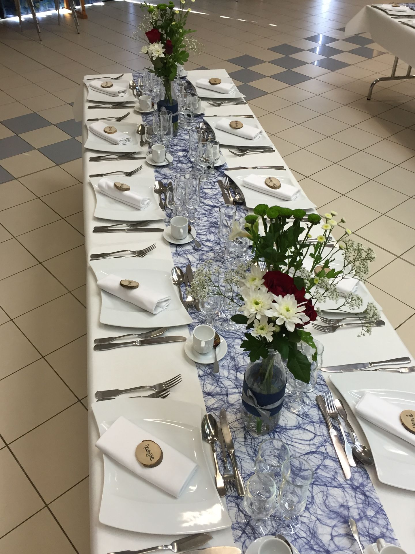 Mariage Salle Azura 2000 table blanche chemin de table bleu marine vase fleurs rouge blanche et feuillage marque place rondin en bois personnalisé