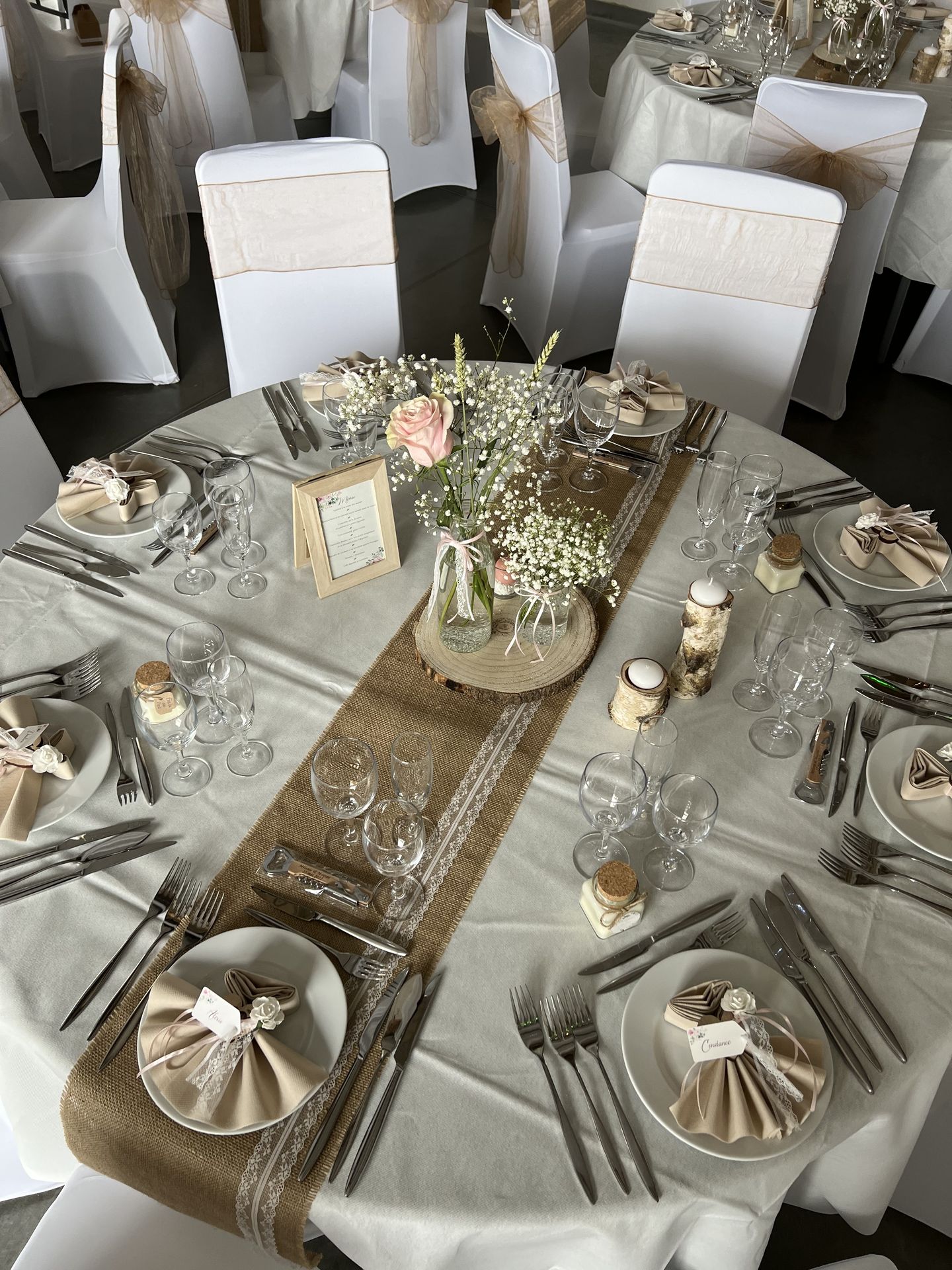 Mariage Salle du Grand Renard table blanche chemin de table sable noeud de chaise sable centre de table rondin en bois fleurs vase transparents serviette sable dentelle bougies bois