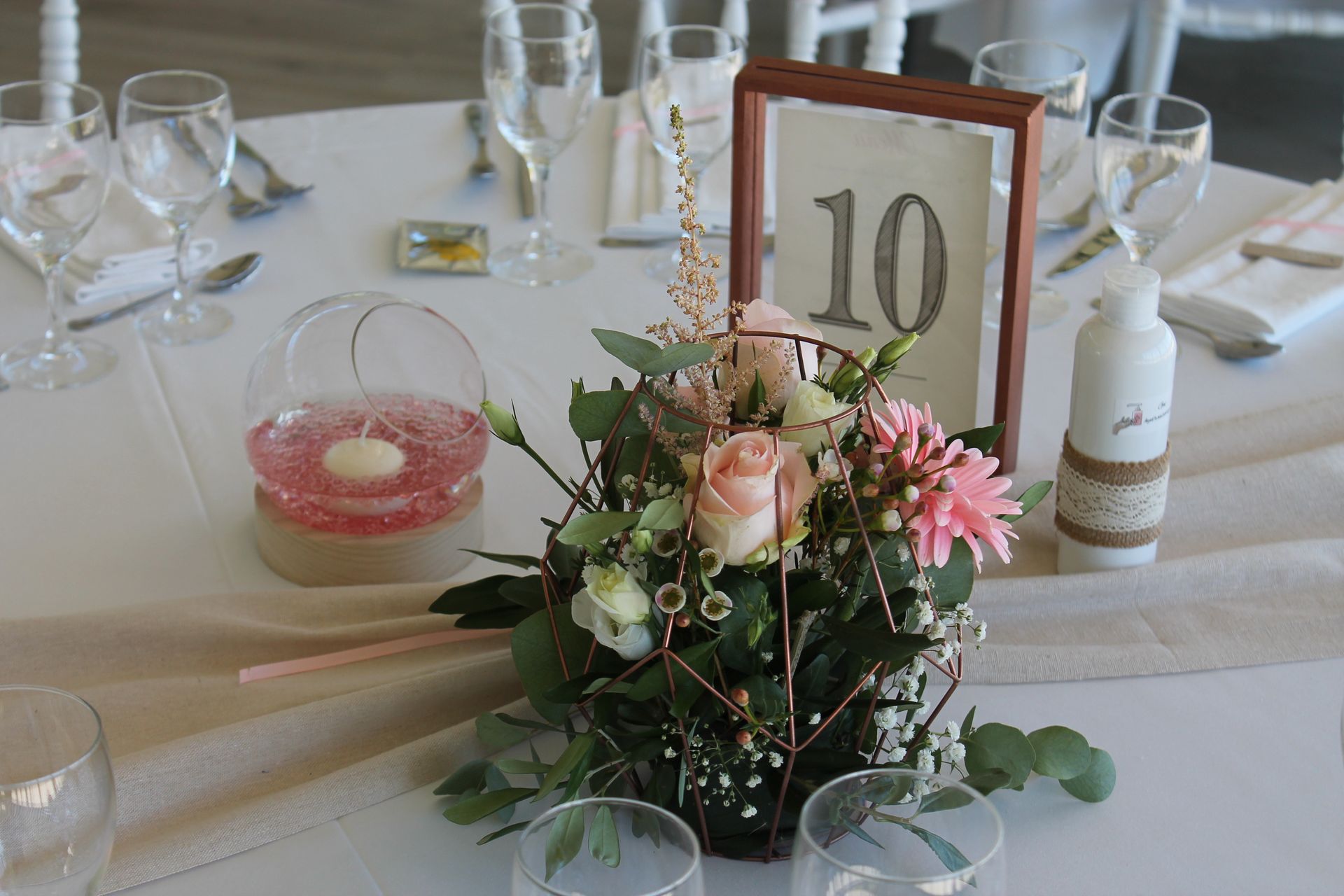 Mariage Domaine de L'Oiselinière table blanche chemin de table sable composition florale et feuillage bougie vase eau rose numéro de table cadre rose