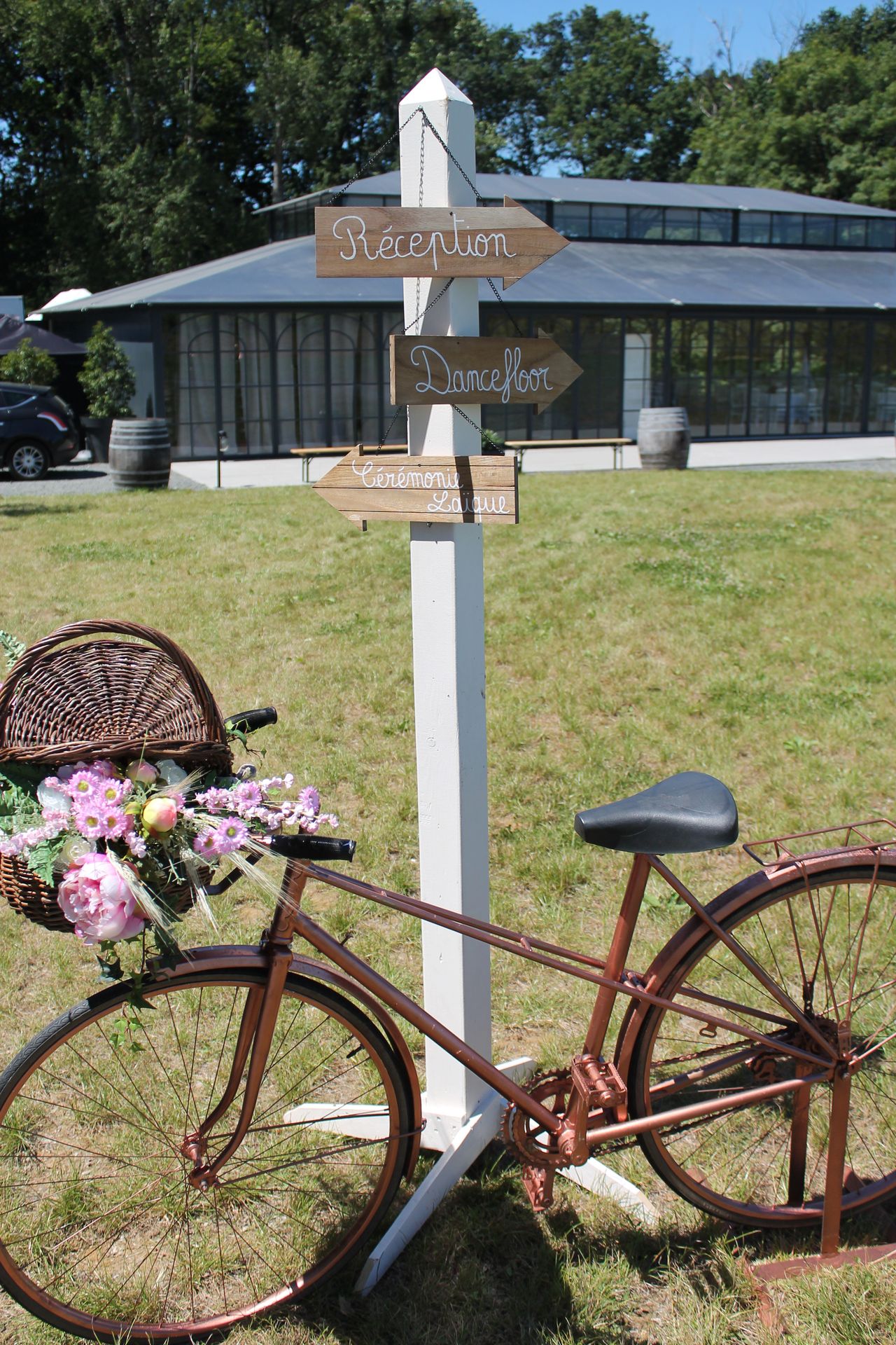 Mariage Domaine de L'Oiselinière décor panneau de direction blanc et bois velo en bronze et fleurs