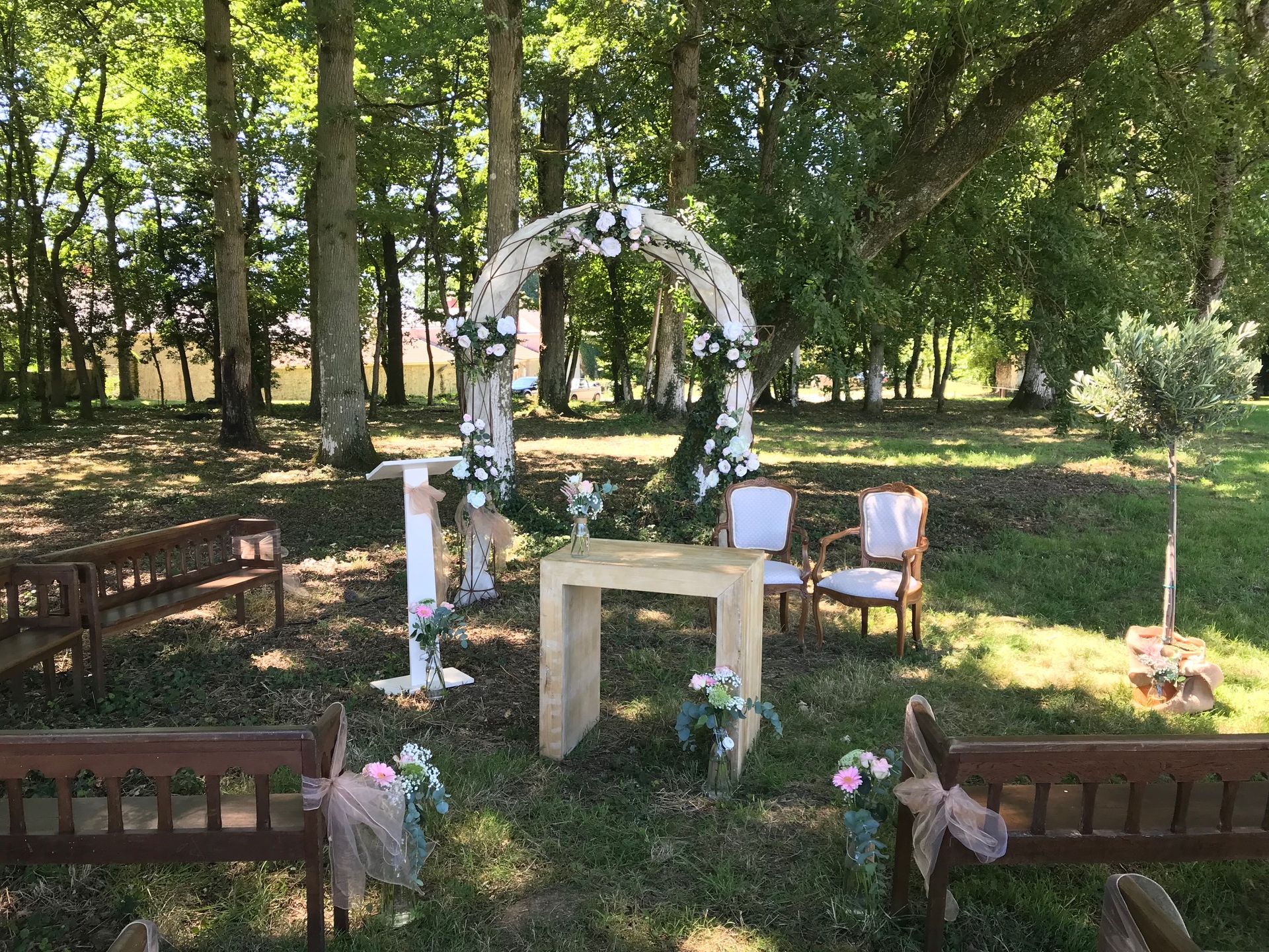 Mariage Domaine de L'Oiselinière arche en métal tissu blanc composition florale banc en bois