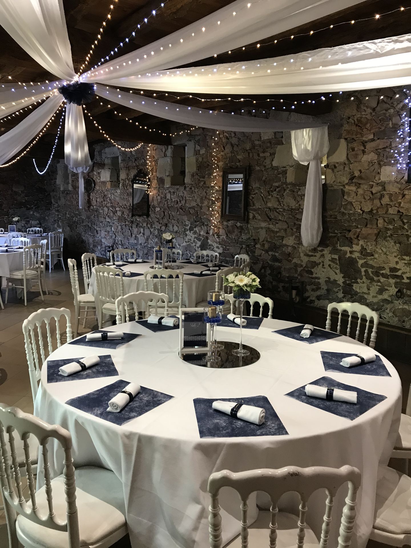 Mariage Château de la Galissonnière plafond tentures blanche leds et fleurs bleu marine table blanche dessous de table bleu marine serviette blanche et noeud bleu marine centre de table miroir rond cadre menu blanc en bois et vase