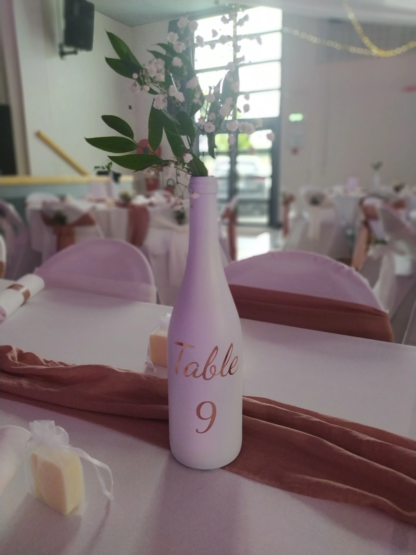 Mariage Salle des Fêtes nom de table bouteille blanche feuillage cadeaux invités savon