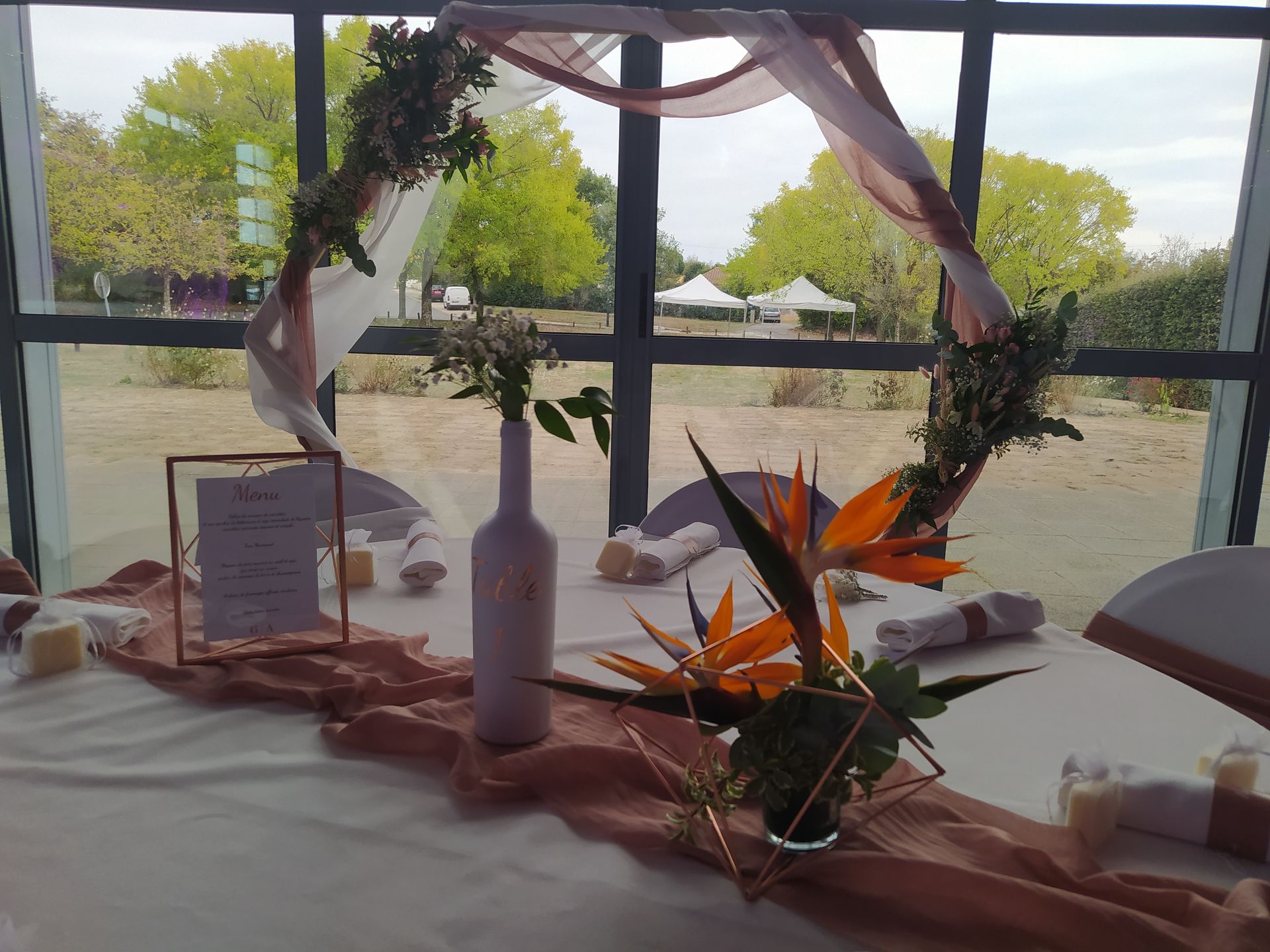 Mariage Salle des Fêtes arche dorée tissu rose et blanc composition florales table blanche chemin de table vieux rose composition fllorale bouteille blanche cadre menu de table rose