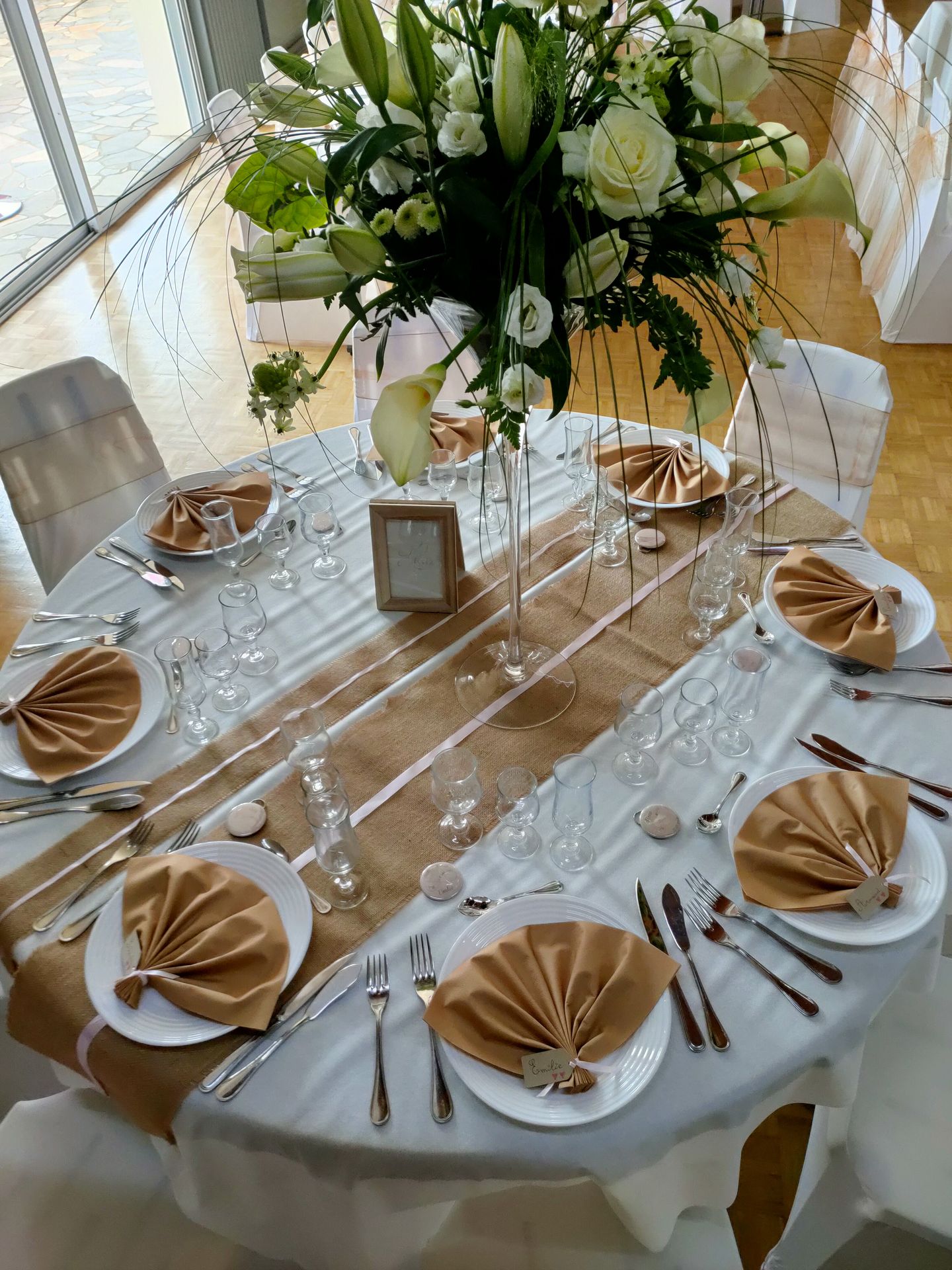 Mariage Salle L'Arc en Ciel table blanche chemin de table sable vase composition florale feuillage fleurs rose serviette sable et marque place menu de table cadre en bois