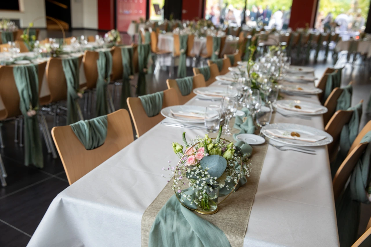 Mariage Salle Collinéa table blanche noeud de chaise vert sauge chemin de table sable composition florale rondin de bois tissu vert sauge