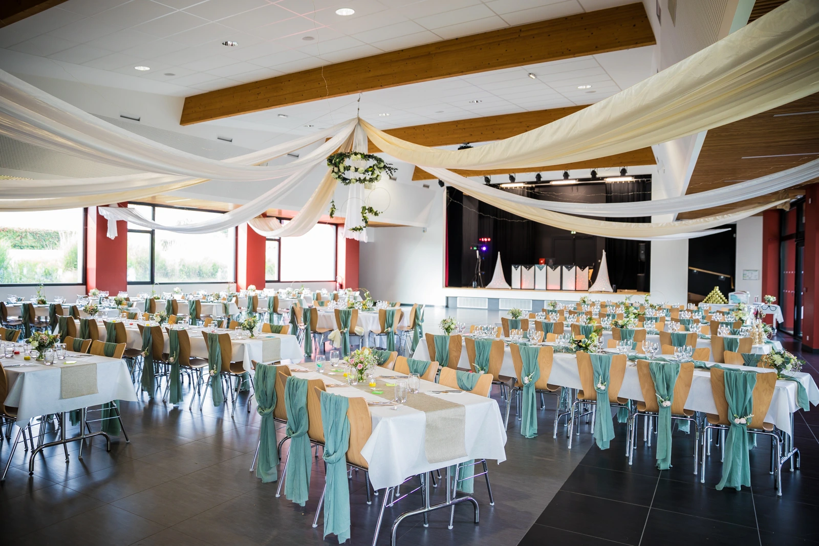 Mariage Salle Collinéa plafond tentures blanche sable leds et couronne de feuillage table blanche noeud de chaise vert sauge chemin de table sable composition florale rondin de bois tissu vert sauge